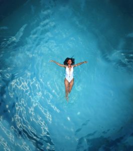 Девушка в закрытом белом купальнике лежит на спине в море, раскинув руки в стороны